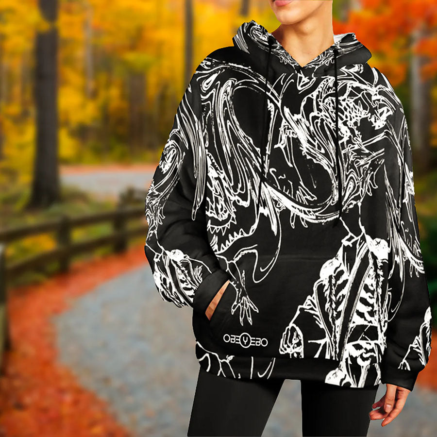 Artistic black and white hoodie featuring intricate designs, worn by a model in a serene autumn forest.